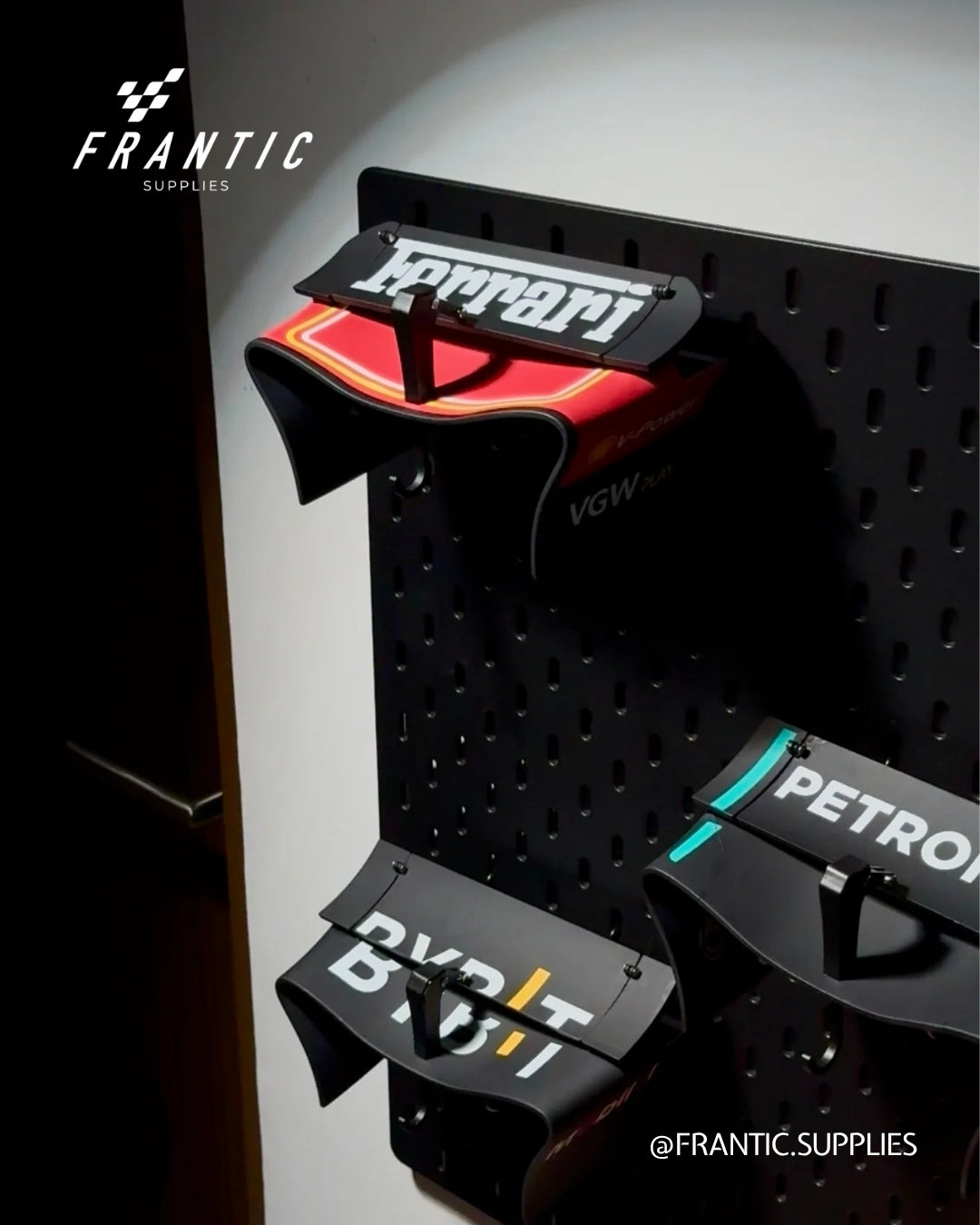 Black pegboard wall with wing-style car keyholder brackets labeled Ferrari, Petron, and DVK, arranged vertically, branded Frantic Supplies.